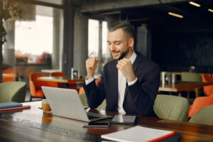 A suited man is seated at a table, working intently on his laptop, embodying a professional atmosphere