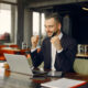 A suited man is seated at a table, working intently on his laptop, embodying a professional atmosphere